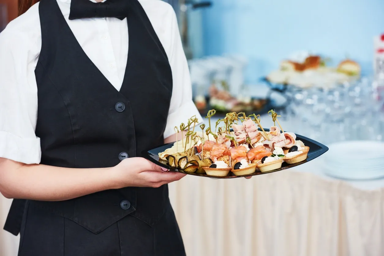 A person holding a tray of food on top of a table.